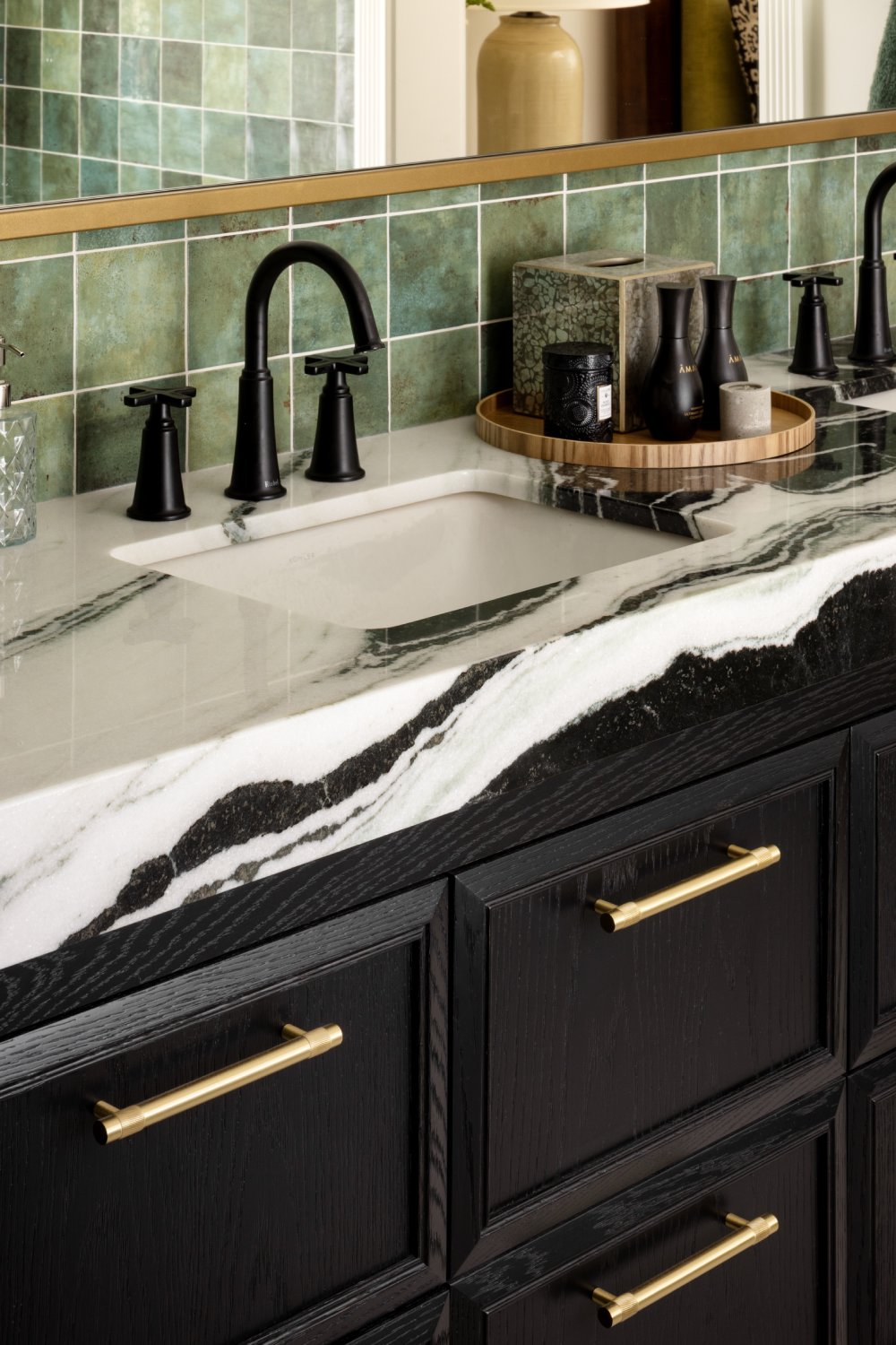 Bathroom vanity with black and white marble countertop, black cabinetry and gold hardware.