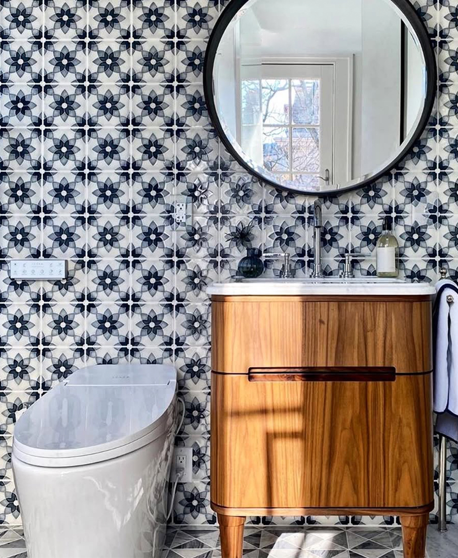 Bathroom with modern toilet, wood cabinet sink stand, and circular mirror against a patterned Pratt Larso tile wall.