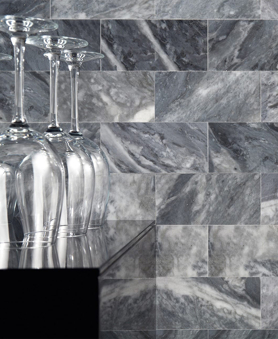 Close up of upside down wine glasses on a glossy black countertop with a grey Stone Partnership tile wall behind it.