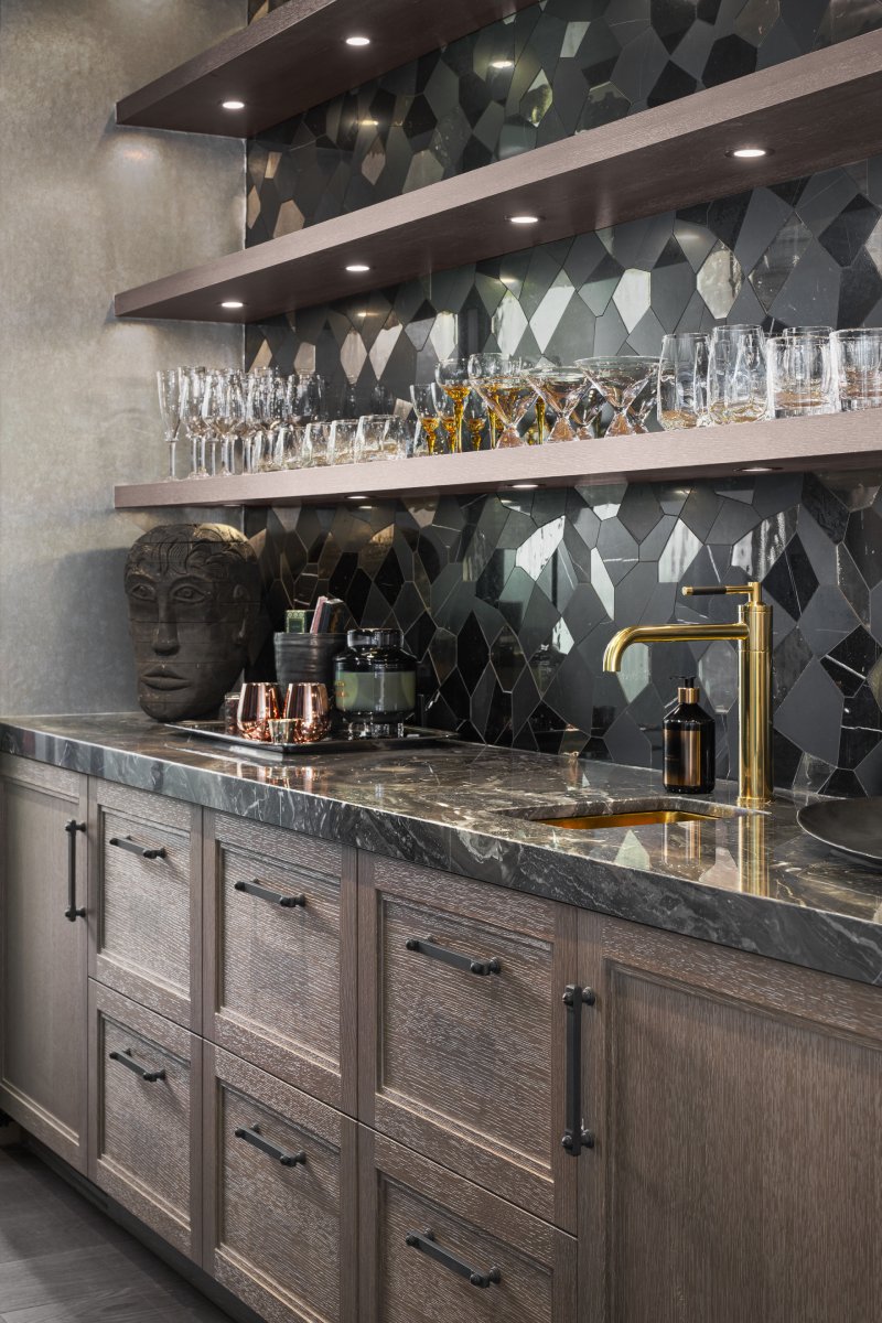 Home bar with open shelving, dark backsplash and brass faucet.